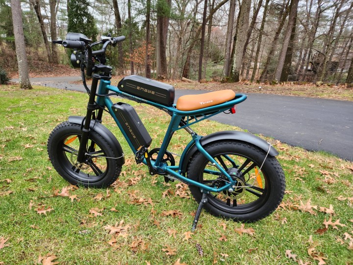 Engwe M20 e-bike left rear three quarter view parked on a lawn next to a steep driveway.